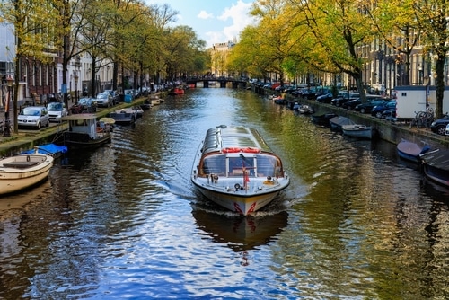 Boats cruising along the scenic canals of Amsterdam, lined with historic Dutch houses and vibrant greenery.