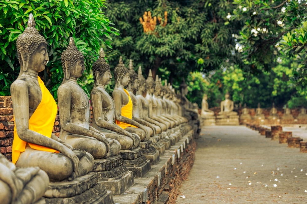 A panoramic view of Ayutthaya Historical Park showcasing ancient temple ruins, prang towers, and a large reclining Buddha statue under a clear blue sky, reflecting the historical and cultural grandeur of the former capital of Siam.